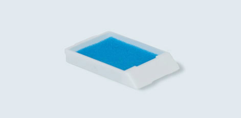 A small, rectangular sponge with a blue, porous surface housed in a white, plastic frame. The sponge is designed for cleaning or absorbing liquids.