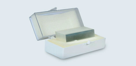 A transparent case with a white base is open, revealing a rectangular bar of soap inside. The soap is a light blue color and sits on a soft, white surface. The case is designed to protect and display the soap.