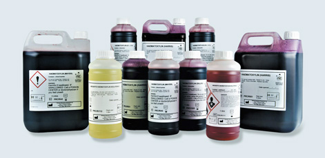 A collection of various containers filled with colored liquids, including canisters and bottles with clear labels. The containers vary in size and color, with warning symbols indicating they contain hazardous materials. The arrangement highlights the variety of contents and emphasizes safety in handling.