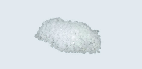 A small mound of white granules, resembling salt or sugar, is displayed against a light background. The granules are round and varied in size, creating a textured appearance.